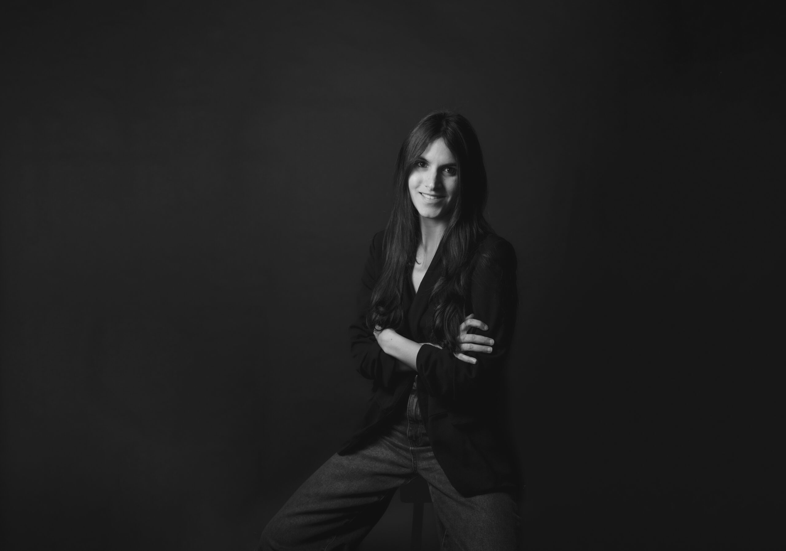 Retrato en blanco y negro de Karen Goncalves, sonriendo con los brazos cruzados sobre fondo oscuro